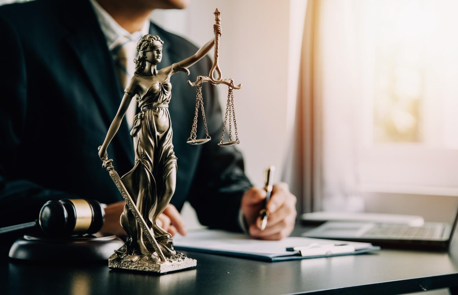 Person writing on a paper next to a lawyers statue